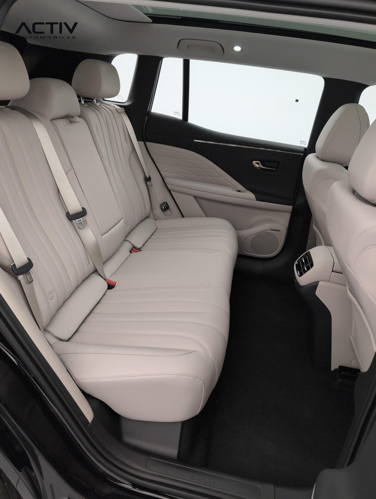Aion V : banquette arrière beige vue par la portière ouverte, avec ceintures et buses d'aération