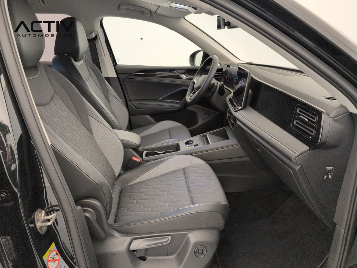 Volkswagen Tiguan : sièges avant en tissu gris et noir, planche de bord et écran vus côté passager