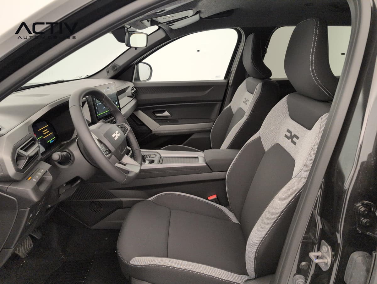 Dacia Bigster Hybrid : sièges avant en tissu gris et noir et poste de conduite vus par la portière