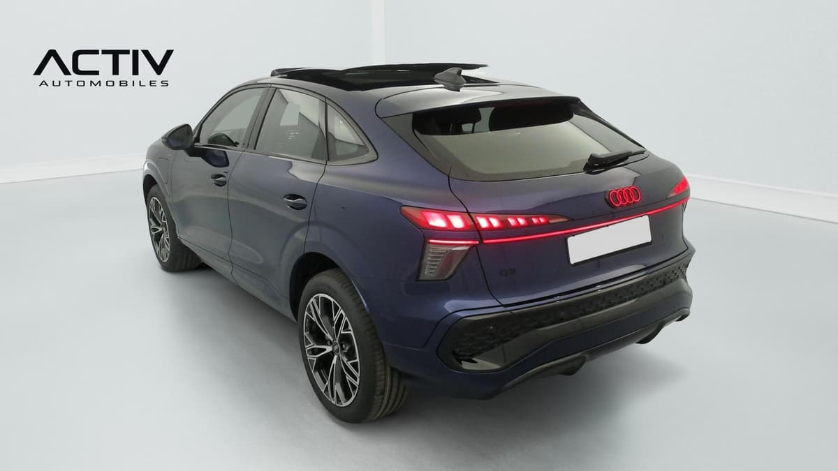 Audi Q3 Sportback Hybride : vue arrière trois quarts gauche, bleu foncé, feux allumés et jantes bicolores