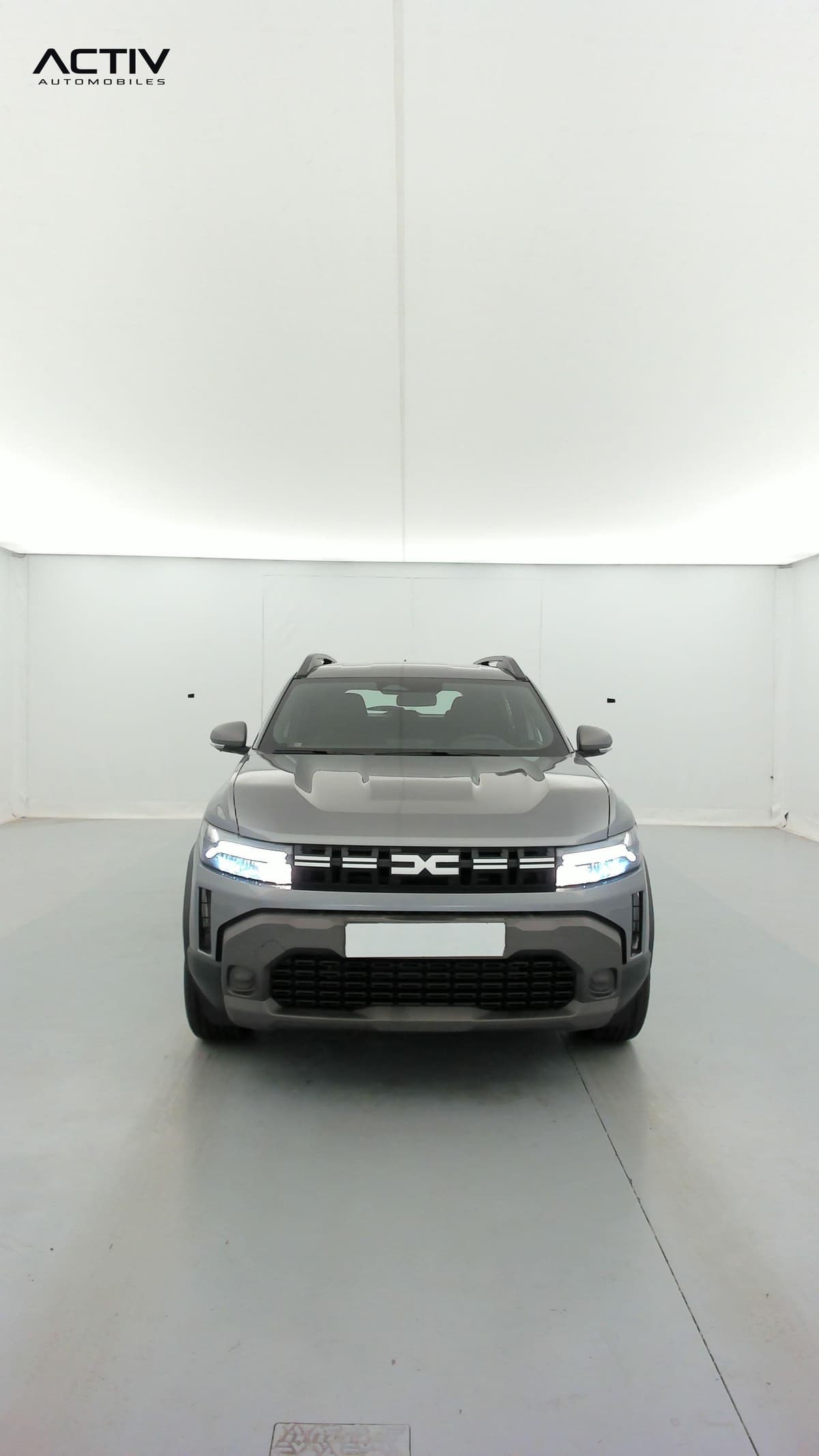 Dacia Duster : face avant grise avec feux allumés et barres de toit