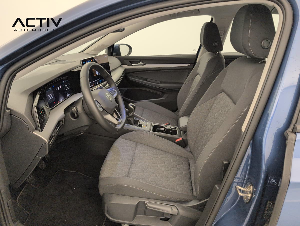 Volkswagen Golf 8 : sièges avant en tissu gris et poste de conduite vus par la portière ouverte