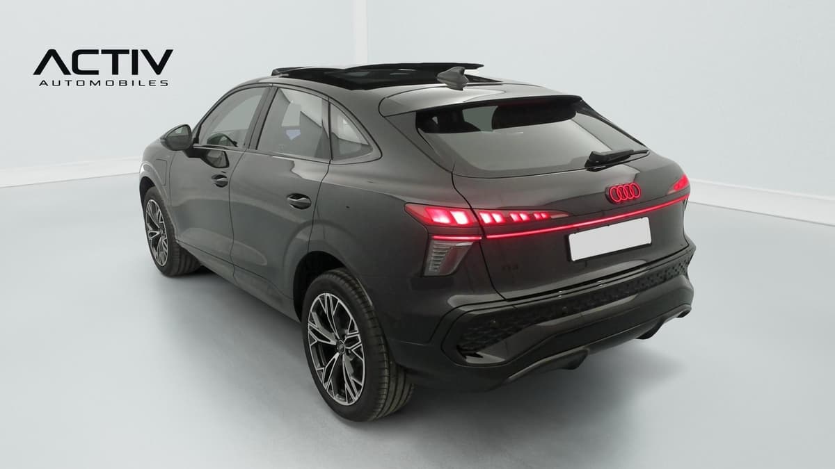 Audi Q3 Sportback Hybride : véhicule vu de l'arrière trois quarts gauche avec feux allumés et jantes bicolores