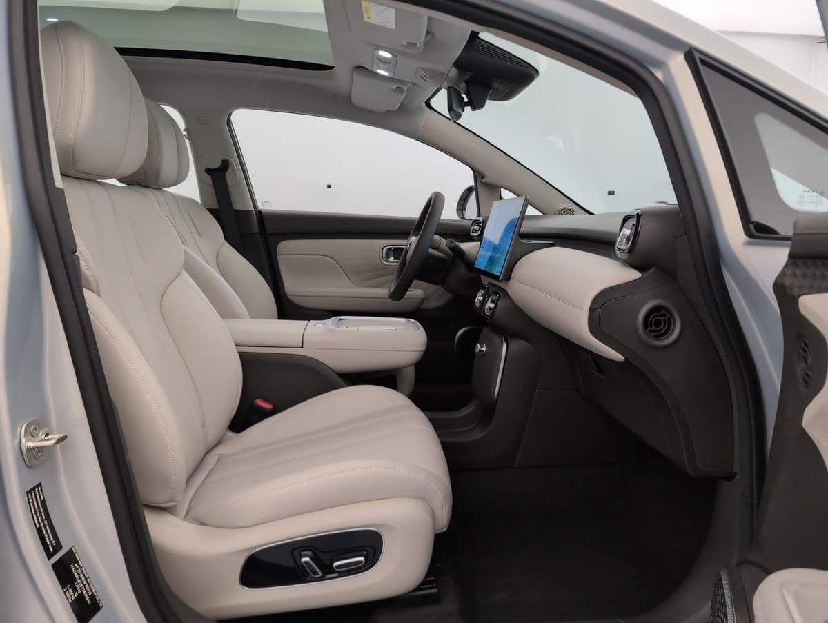 Aion UT : habitacle avant côté passager avec siège beige, volant et écran central