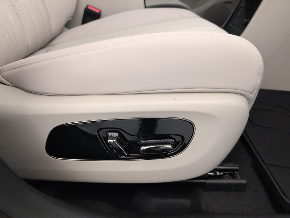 Aion V : côté d'un siège avant beige avec commandes de réglage électrique et tapis en caoutchouc
